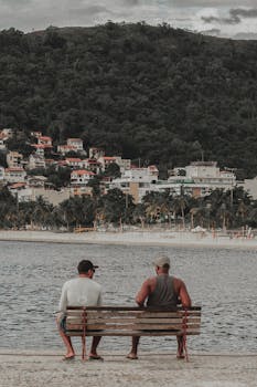 成熟男性坐在长凳上悠闲聊天的背影，与山上的小镇遥相呼应