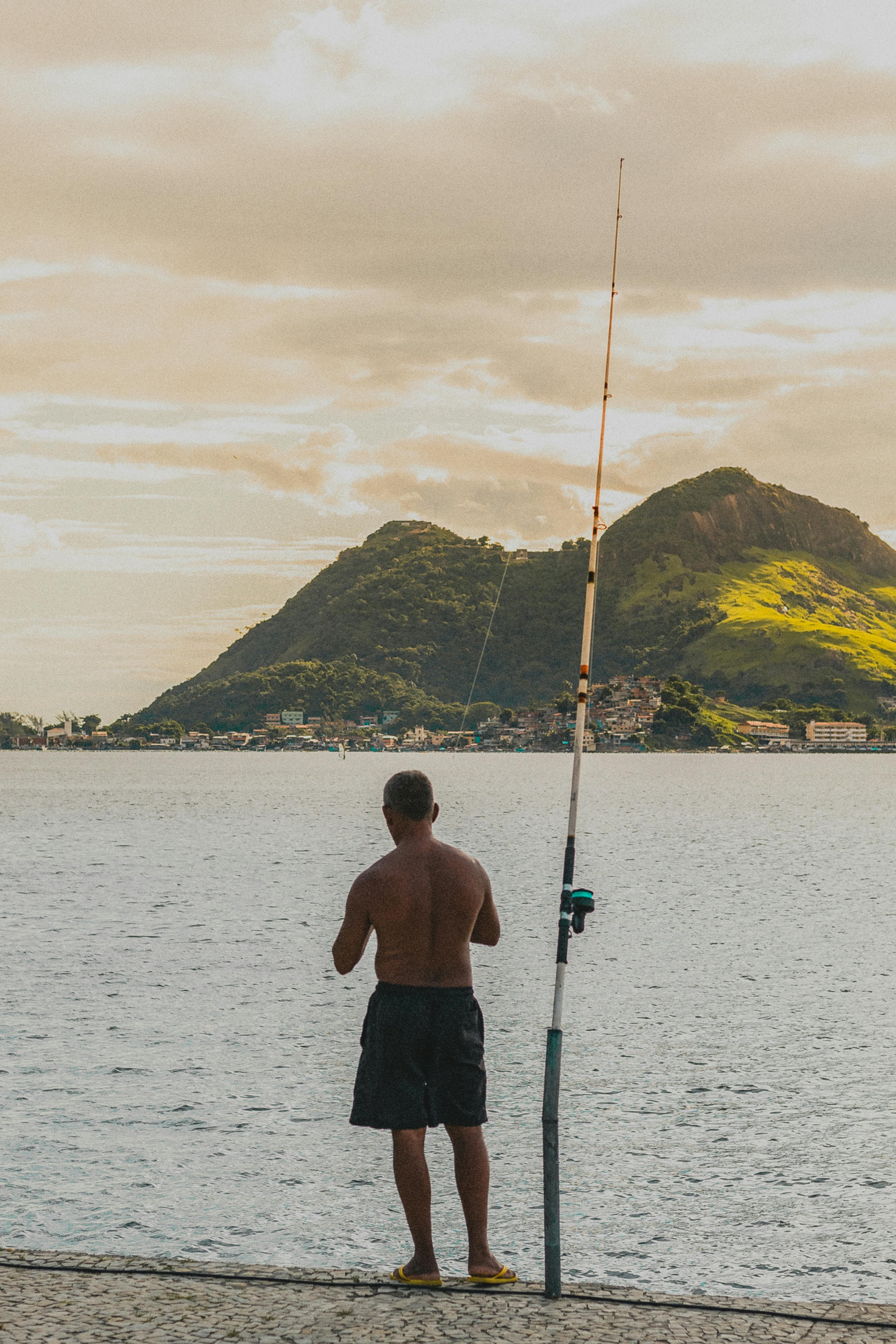 unrecognizable fisherman on seashore in sundown