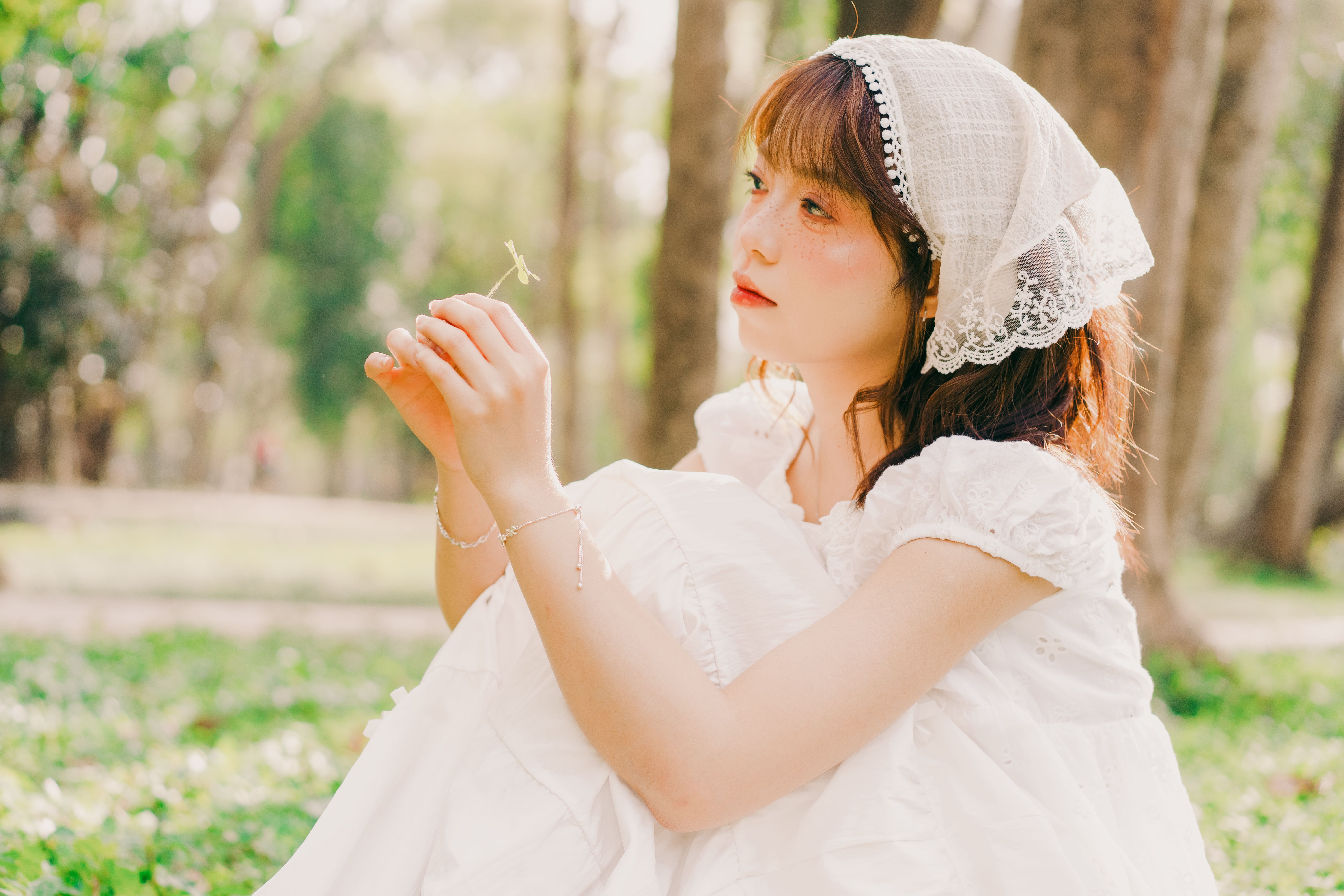Portrait of a young woman in a lace dress enjoying a sunny day in a Hanoi park.