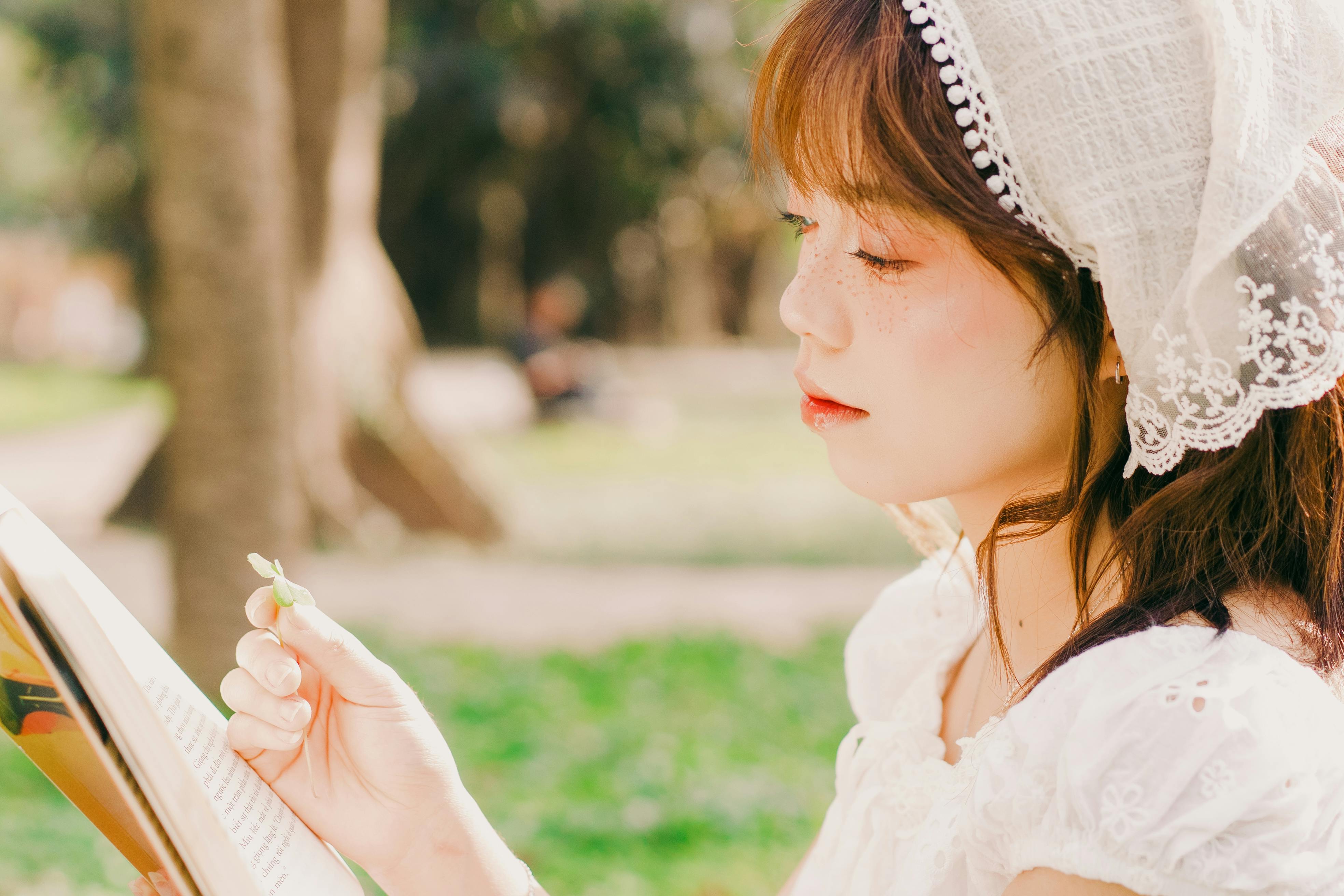Young woman in lace dress reads outdoors, enjoying a serene day in Hanoi park.