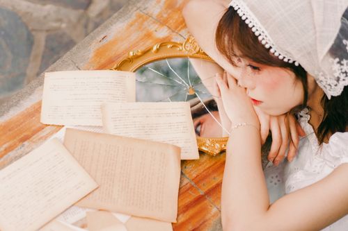 Free A young woman leans on a table with vintage books and a cracked mirror, reflecting her thoughtful expression. Stock Photo