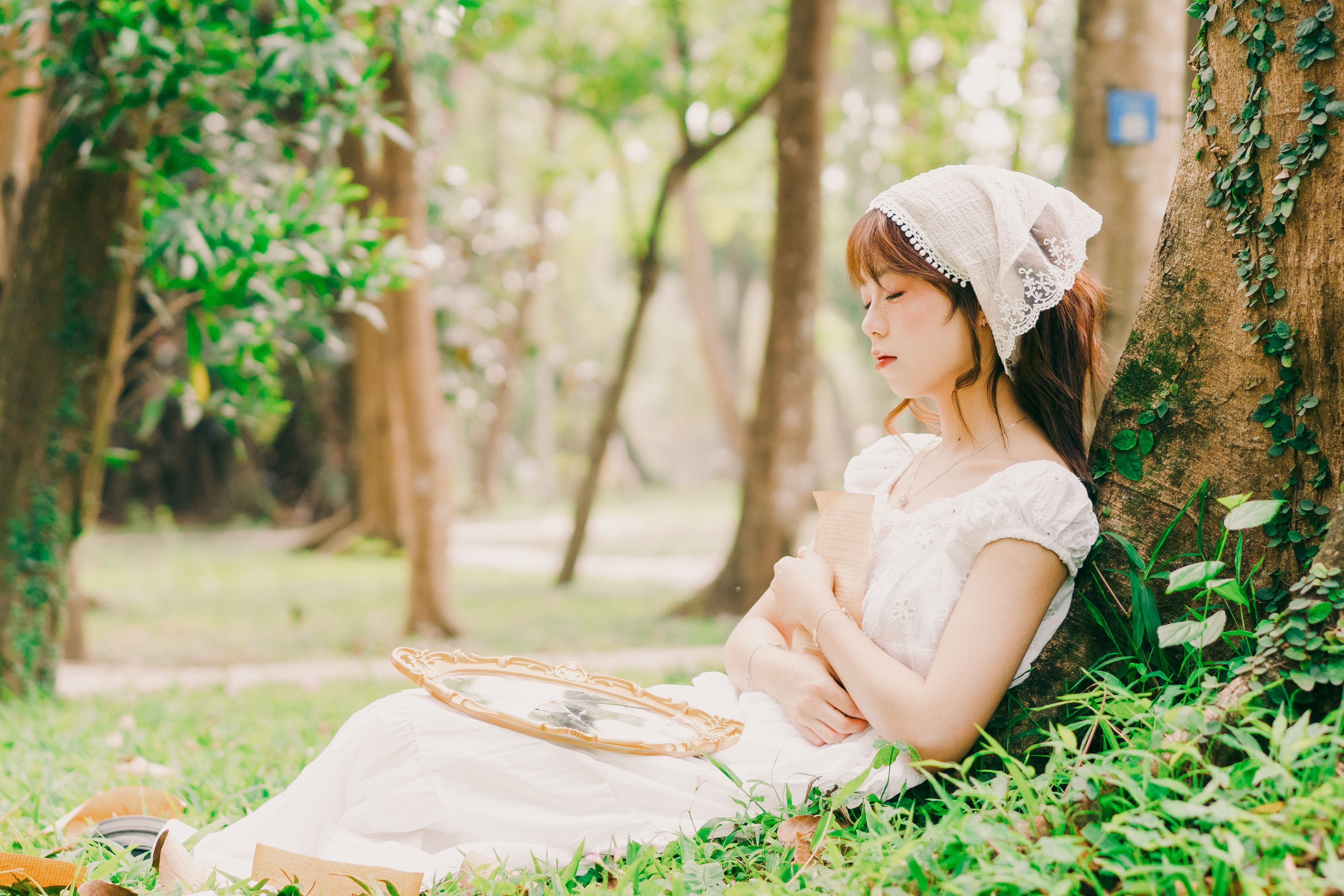 A young woman in traditional attire resting against a tree in a serene Hanoi park.