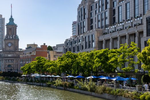 Scenic view of a historic clock tower and riverside promenade with lush green trees in urban setting.