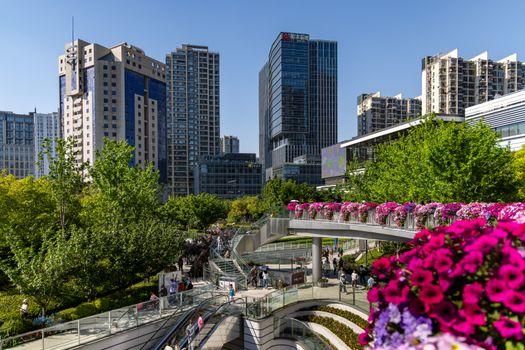 Lush urban park with modern skyscrapers, vibrant flowers, and people enjoying a sunny day.