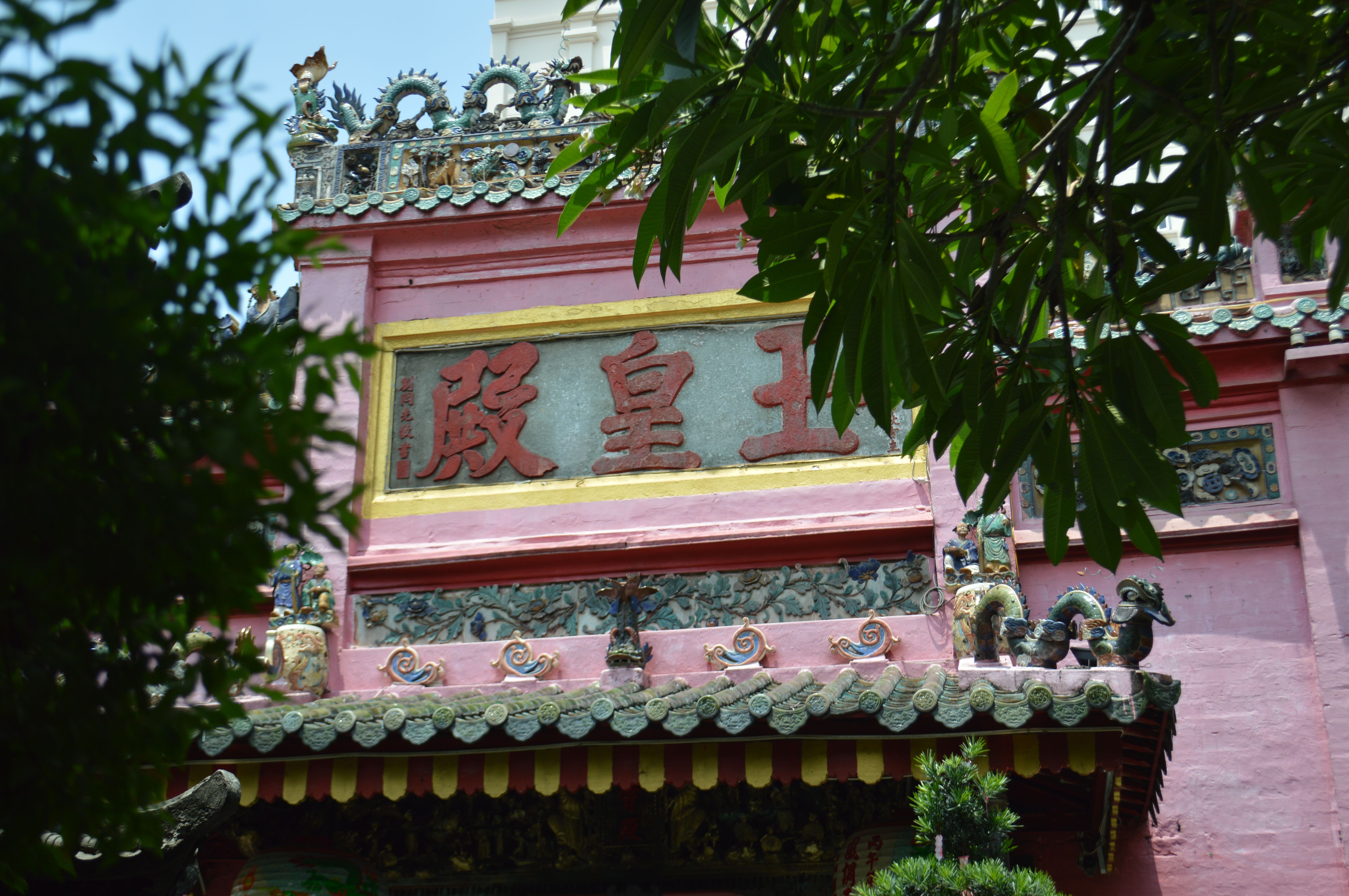 Close-up view of a vibrant Chinese temple façade with intricate designs and Chinese characters, surrounded by lush greenery.