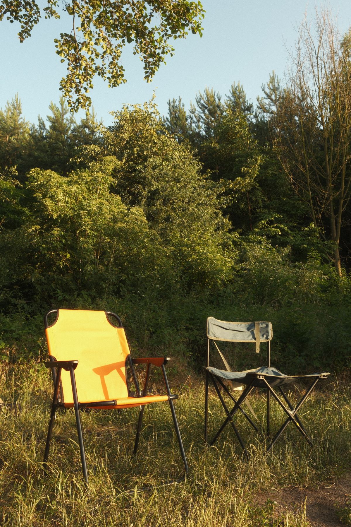 Two folding camping chairs in a sunny forest clearing