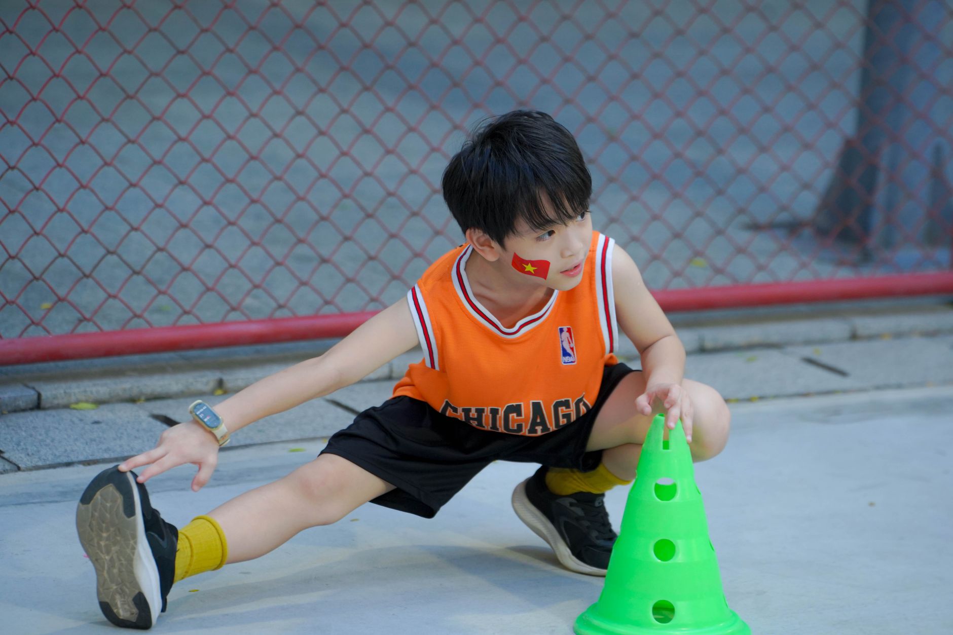 A young boy stretches during an outdoor sports practice, wearing a basketball jersey.