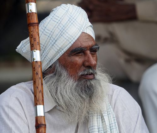 Free Close-up of an elderly man wearing a turban and holding a cane. Introspective and serene expression. Stock Photo