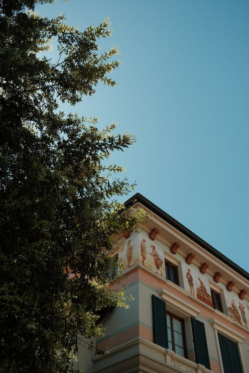 Free Elegant building facade in Milan with artistic frescoes and tree in foreground, under clear blue sky. Stock Photo