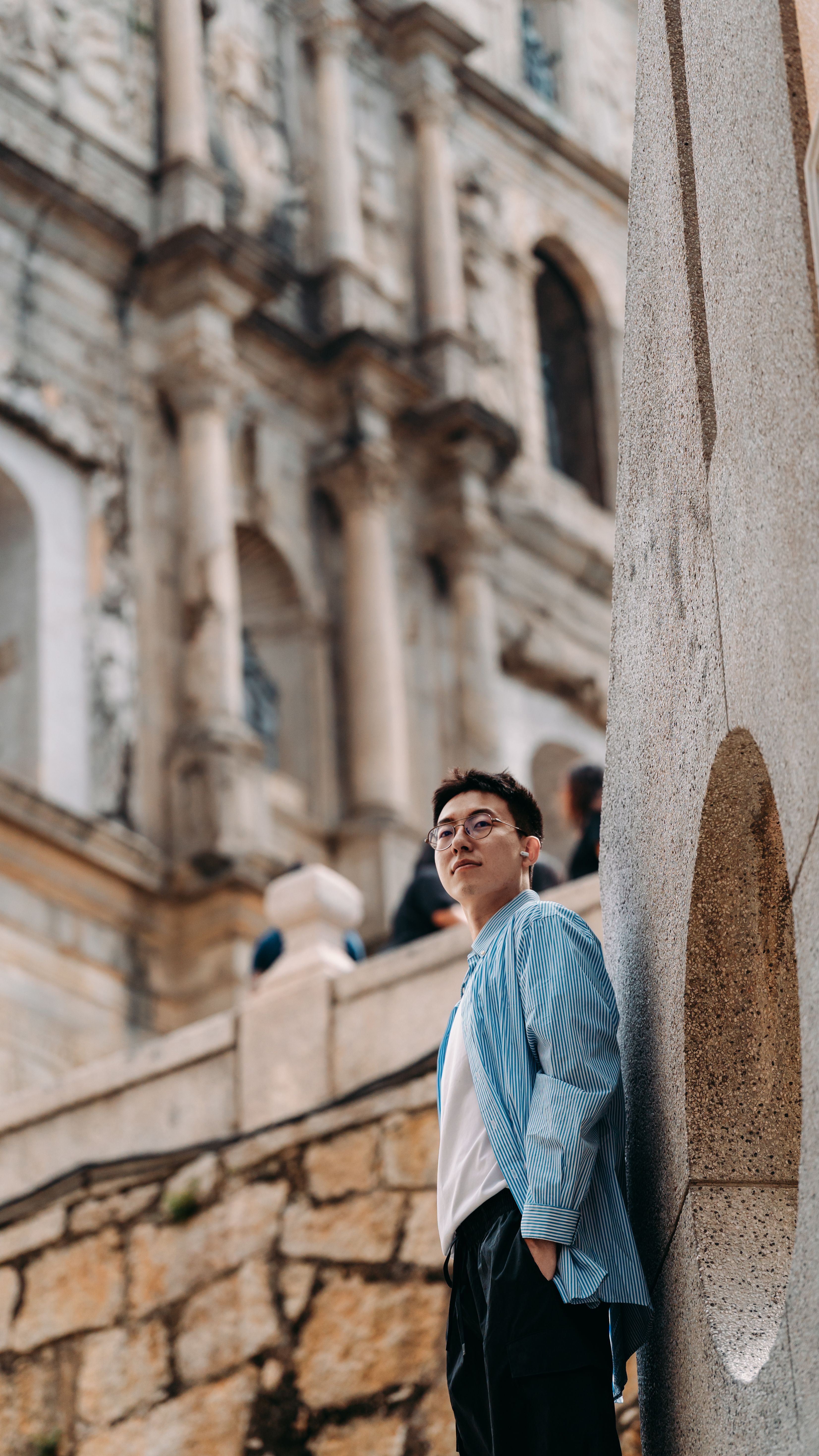 Man standing by ancient stone wall, contemplating near monumental architecture.