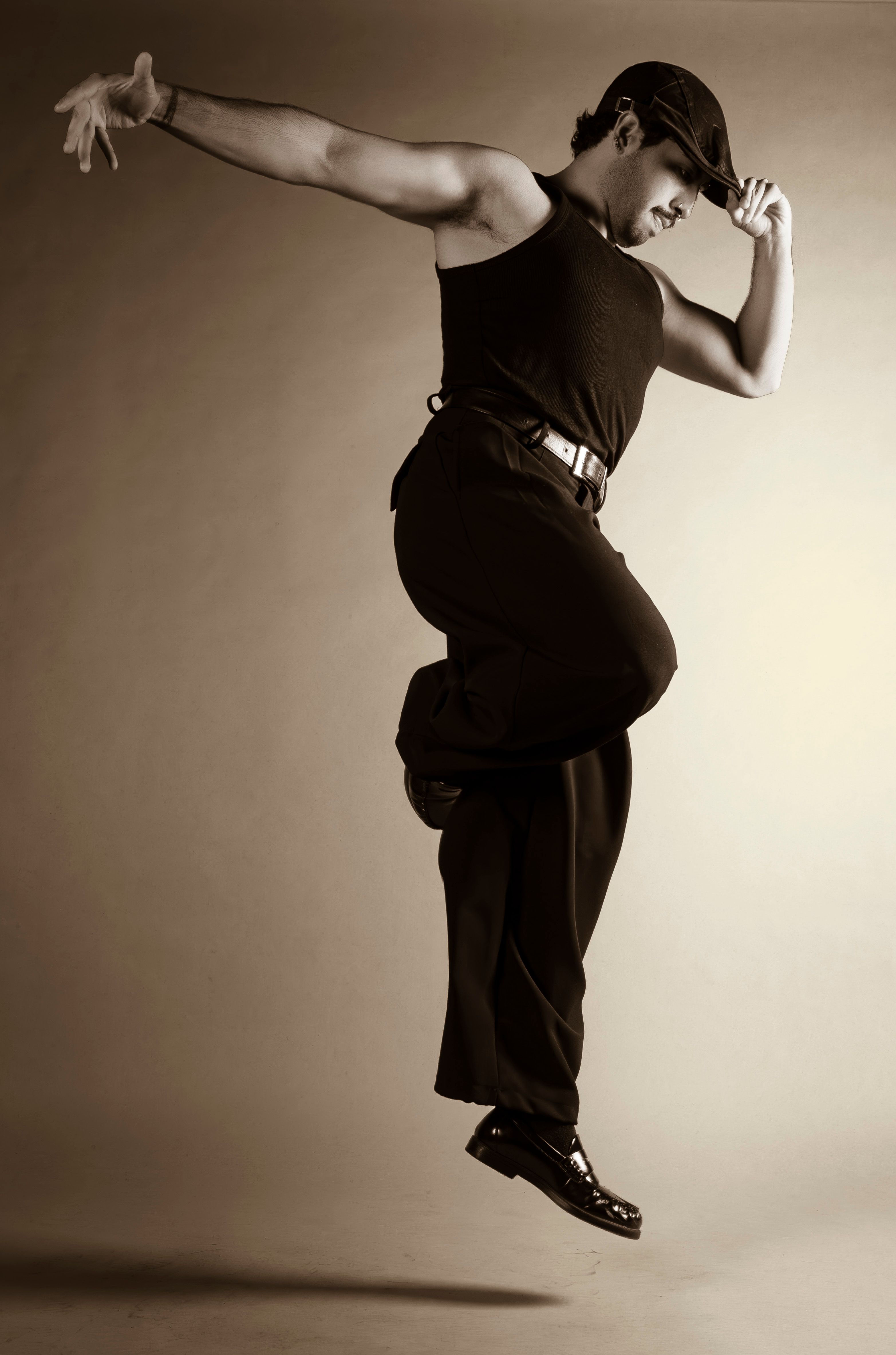 Energetic dancer in mid-air leap wearing a hat and black attire, captured in sepia tone.