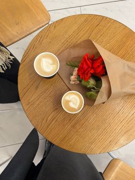 Top view of coffee cups and a rose bouquet on a wooden table, perfect for a romantic date.
