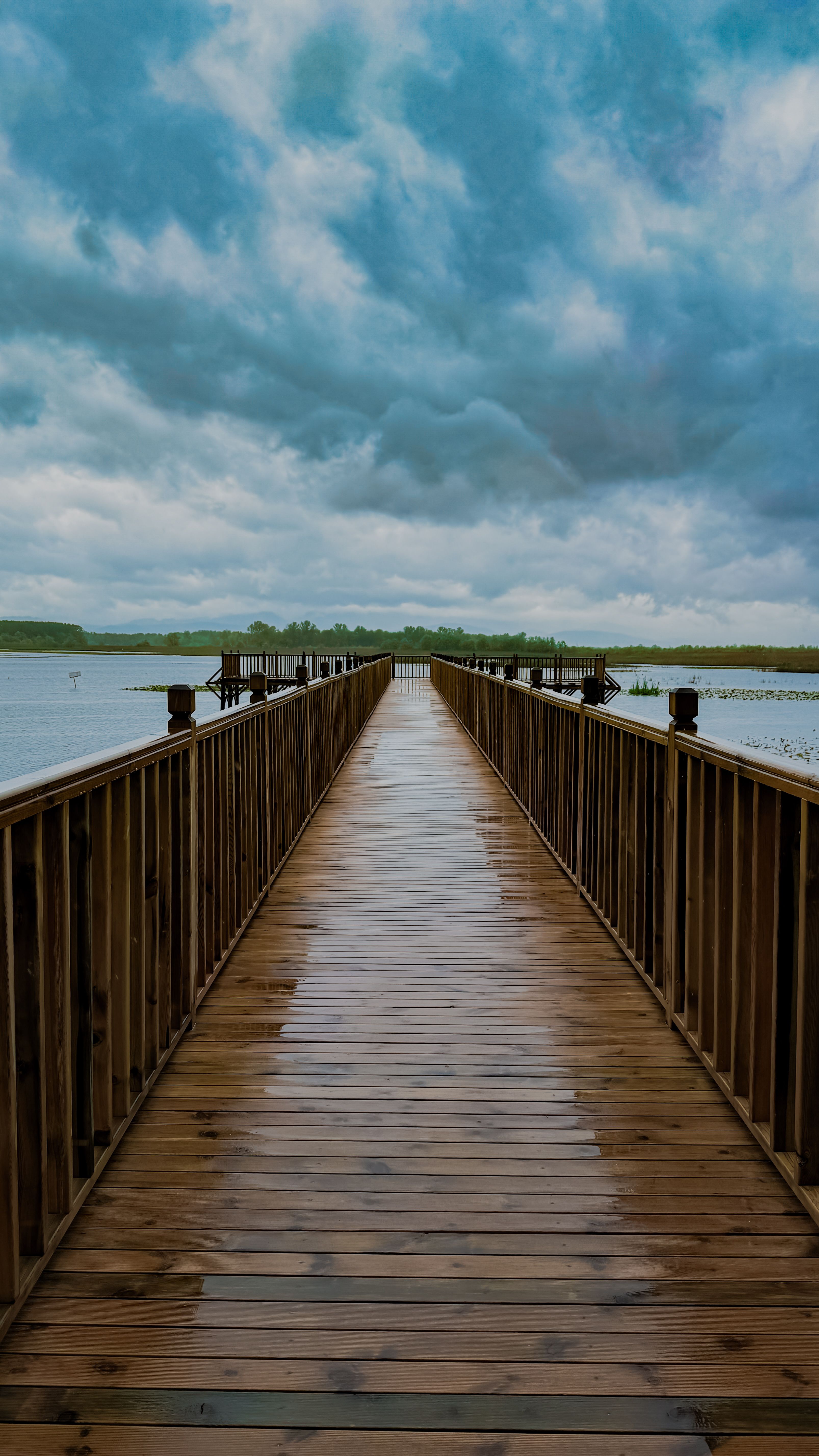 A dramatic cloudy sky looms over a wooden boardwalk leading to a serene lake in Türkiye.