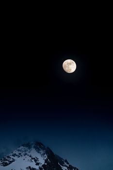 A beautiful full moon shining above snow-capped mountains in Les Belleville, France.