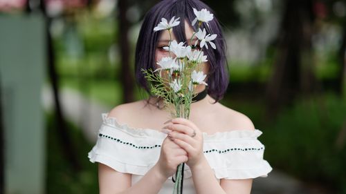 Free A cosplayer with dyed hair poses outdoors, holding white flowers, creating a serene spring scene. Stock Photo