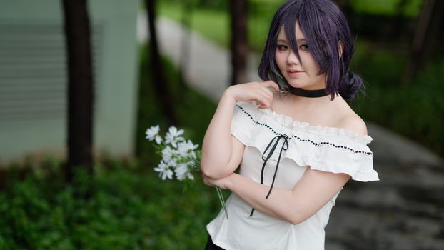 A woman in cosplay costume poses outdoors holding flowers. Vibrant and youthful fashion.