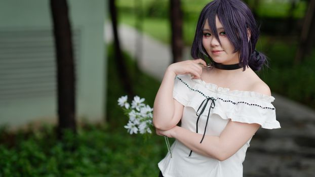 Cosplayer poses with flowers in a serene outdoor setting in Vietnam.