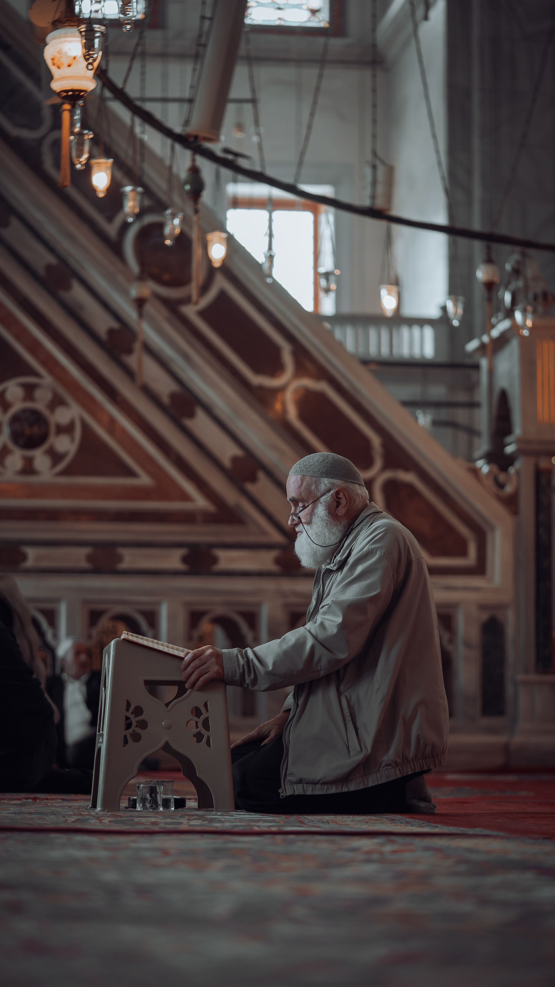 Elderly man engaged in prayer inside a beautifully lit mosque in Istanbul, Türkiye.