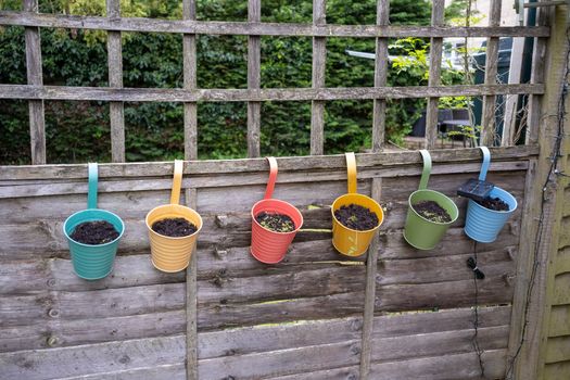 Vibrant hanging pots with soil on a wooden fence in a garden, creating a cheerful outdoor scene.