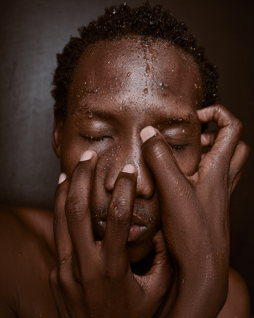 Free Expressive close-up of a man with water drops on his face, hands covering. Stock Photo