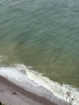 Aerial view of two people walking along a pebble beach with waves lapping the shore.