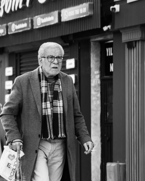 Free Elderly man walking with shopping bag, wearing checkered scarf and glasses. Stock Photo
