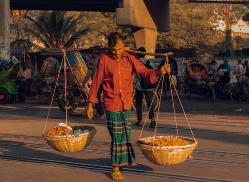 Free A street vendor carries goods in baskets on a yoke in a bustling urban setting. Stock Photo