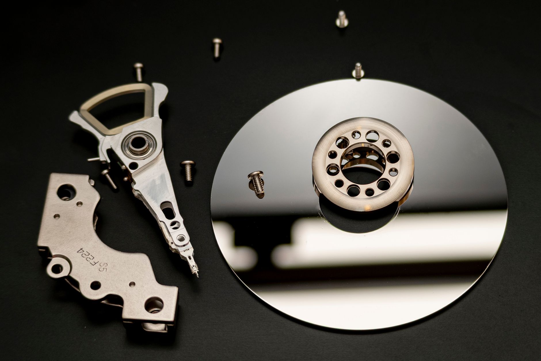Close-up of dismantled hard drive parts with a reflection on a black surface, showcasing intricate mechanical details.