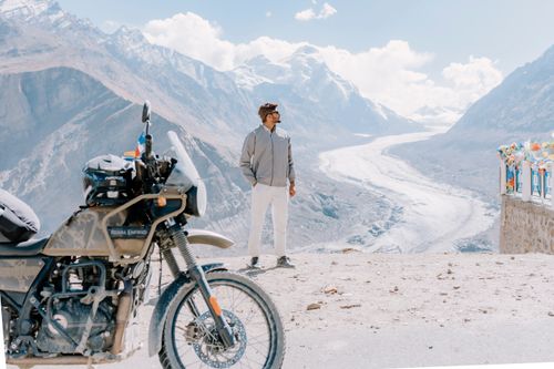 Free Man on mountain road with motorcycle and scenic Himalayan glacier backdrop. Stock Photo