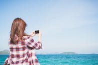 一个女人用她的智能手机在晴朗的天空下拍摄了一张海洋的照片