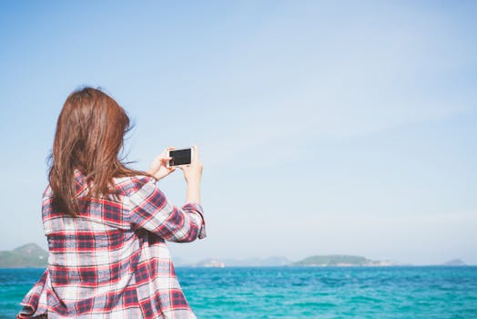 一个女人用她的智能手机在晴朗的天空下拍摄了一张海洋的照片