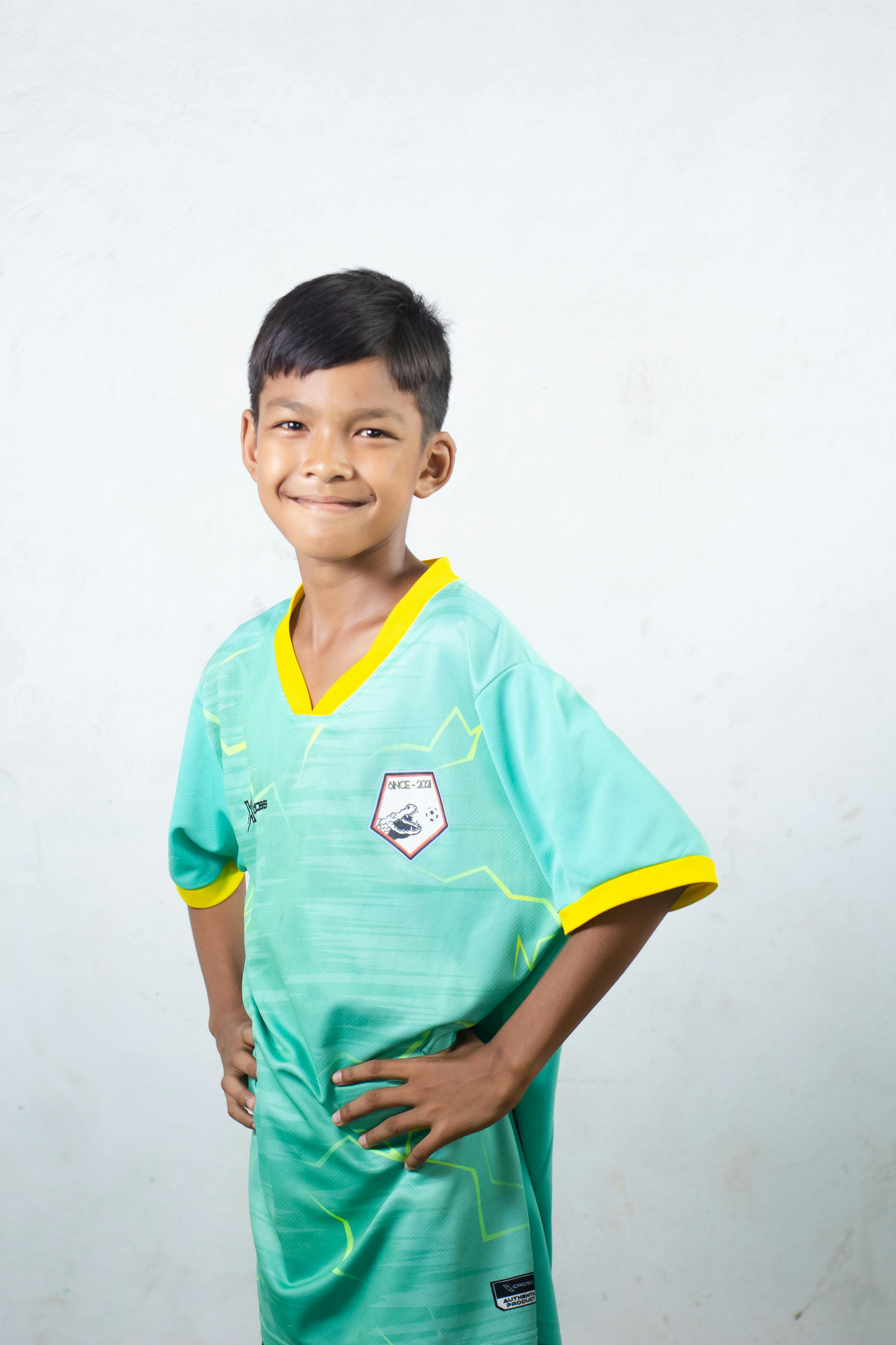 Young boy smiling confidently while posing in a soccer jersey indoors.