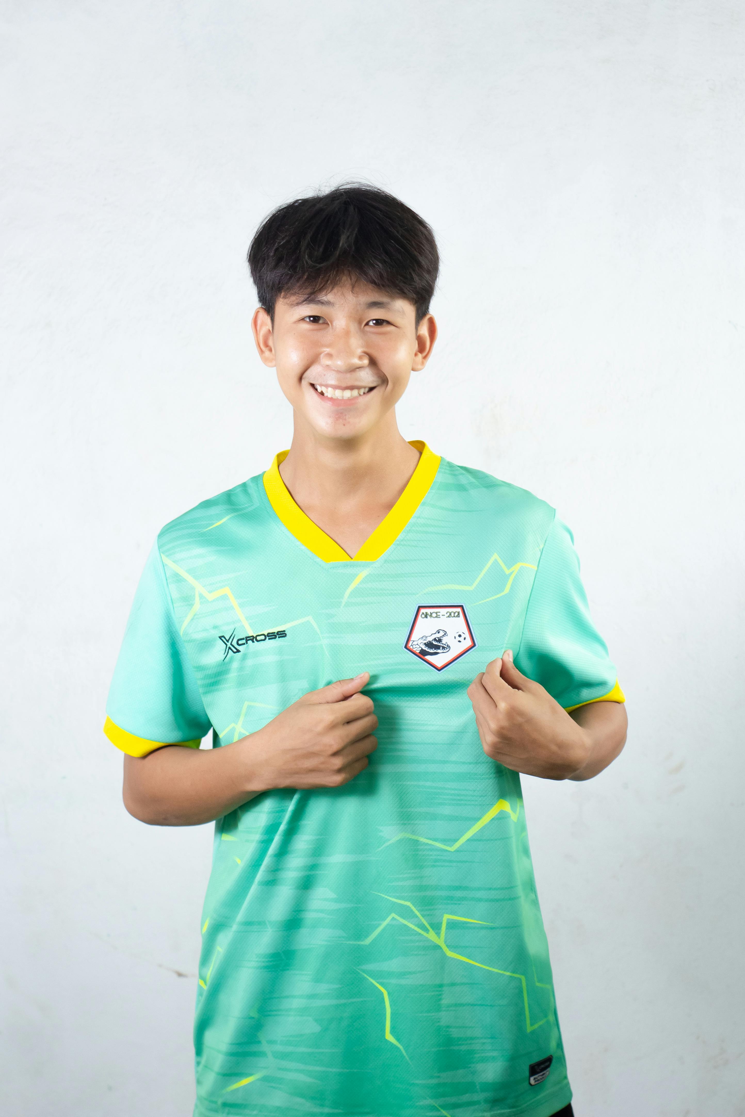 Portrait of a young man smiling, wearing a green sports jersey, pointing at logo.