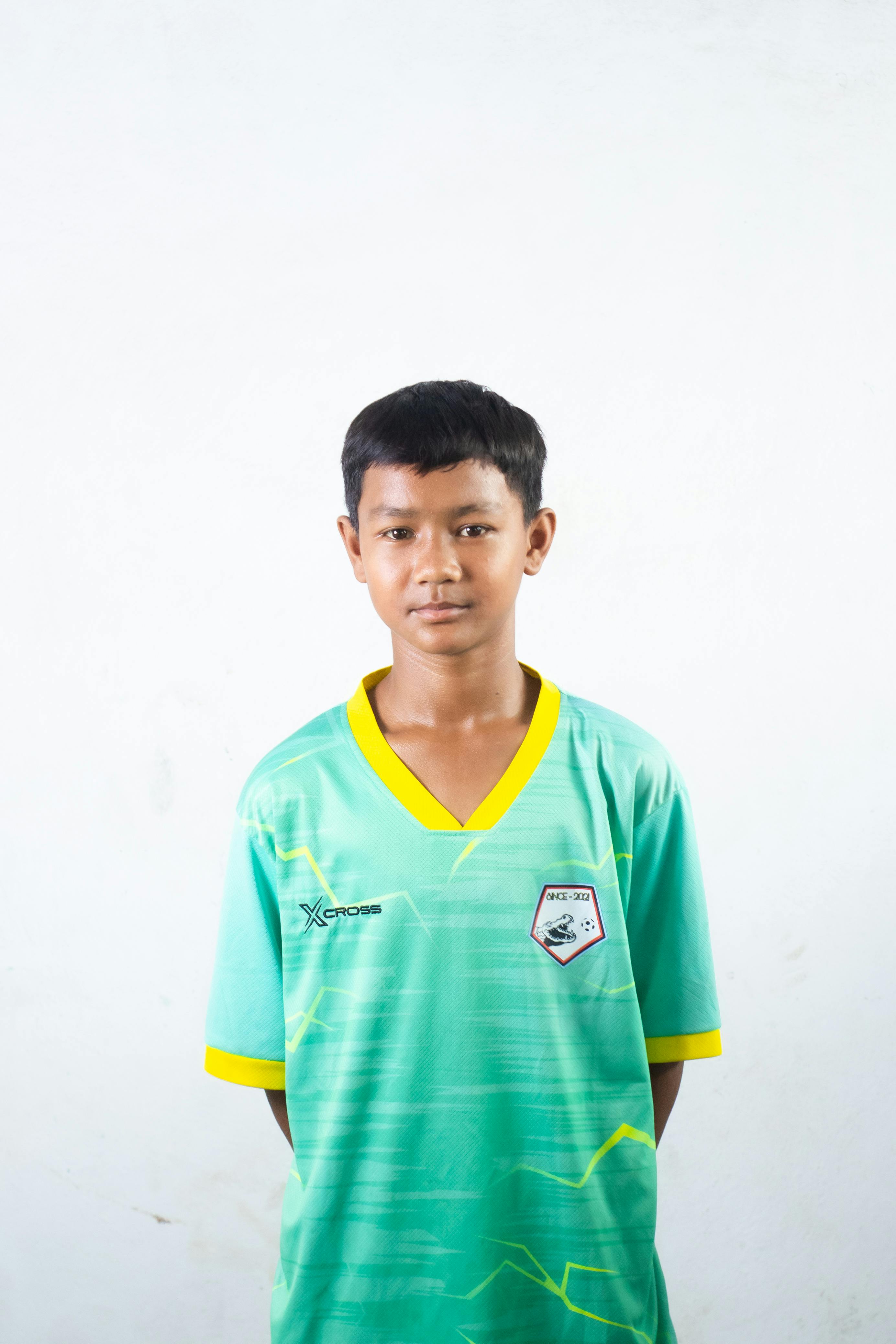 A young boy stands confidently in a green sports jersey against a white background. Ideal for youth sports and portraits.