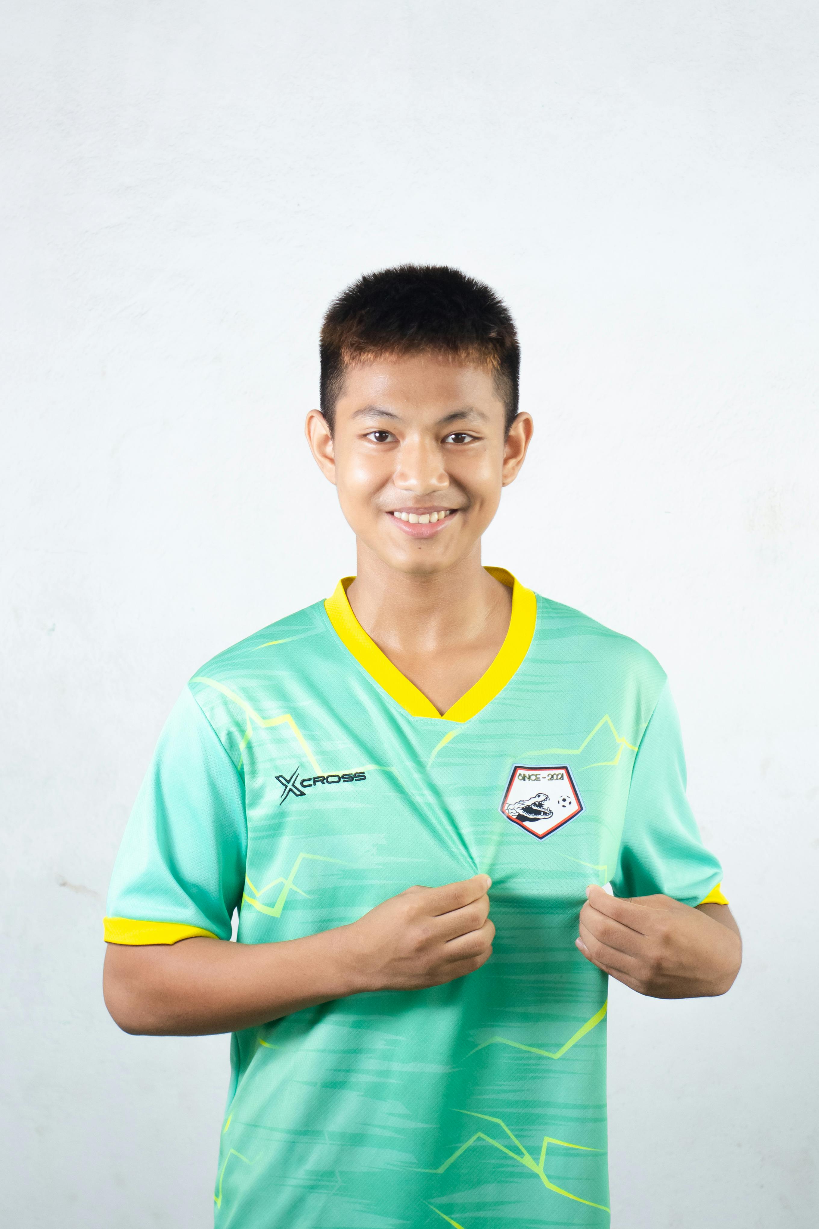 Portrait of a teenage boy wearing a green sports jersey, smiling confidently indoors.