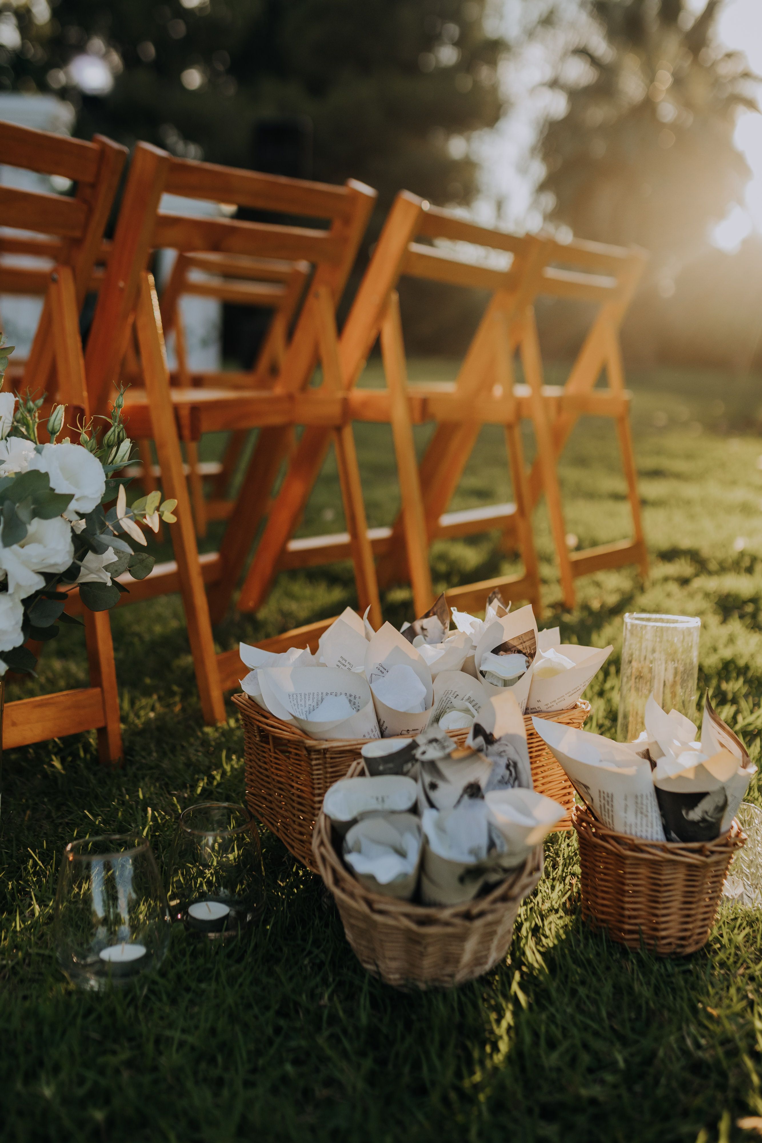 Charming outdoor wedding scene with wooden chairs, wicker baskets, and soft sunset lighting.