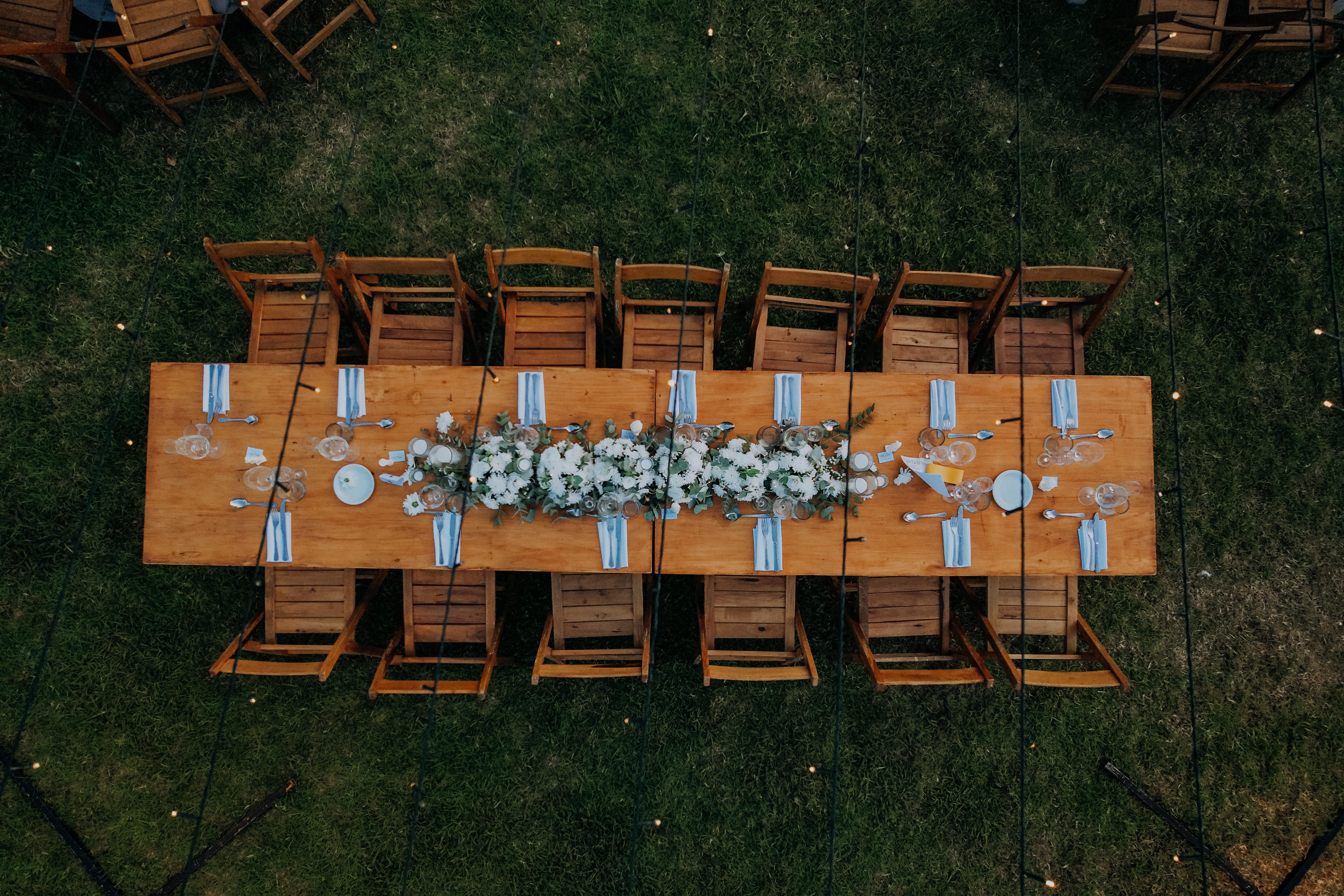 Elegant outdoor rustic wedding reception table setup with floral centerpieces, aerial view.