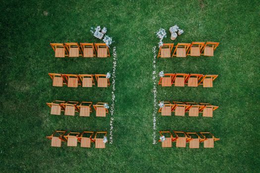 Drone shot of a wedding seating arrangement with orange chairs on green grass.