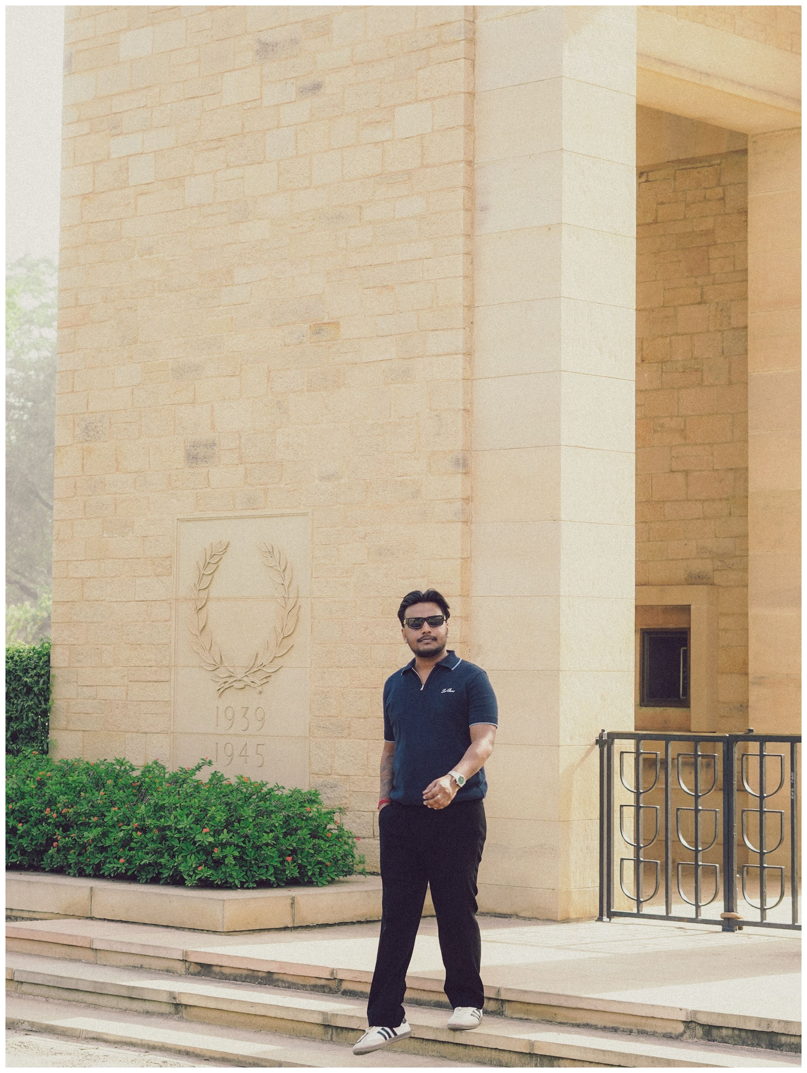 Man posing outside a stone monument with a wreath engraving. Casual and contemplative.