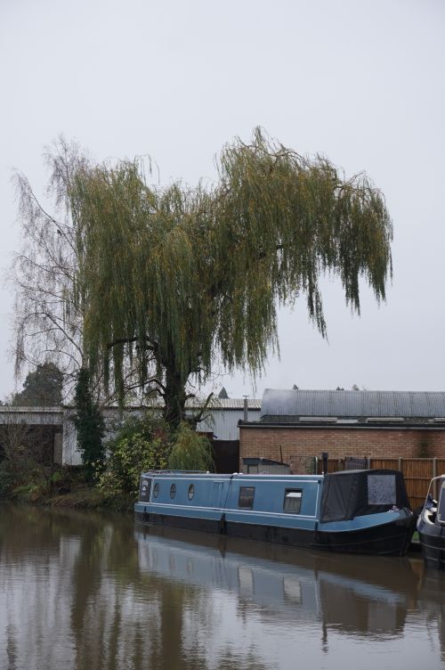 Free Serene canal with houseboat and weeping willow in Warwick, UK, captured on a cloudy day. Stock Photo