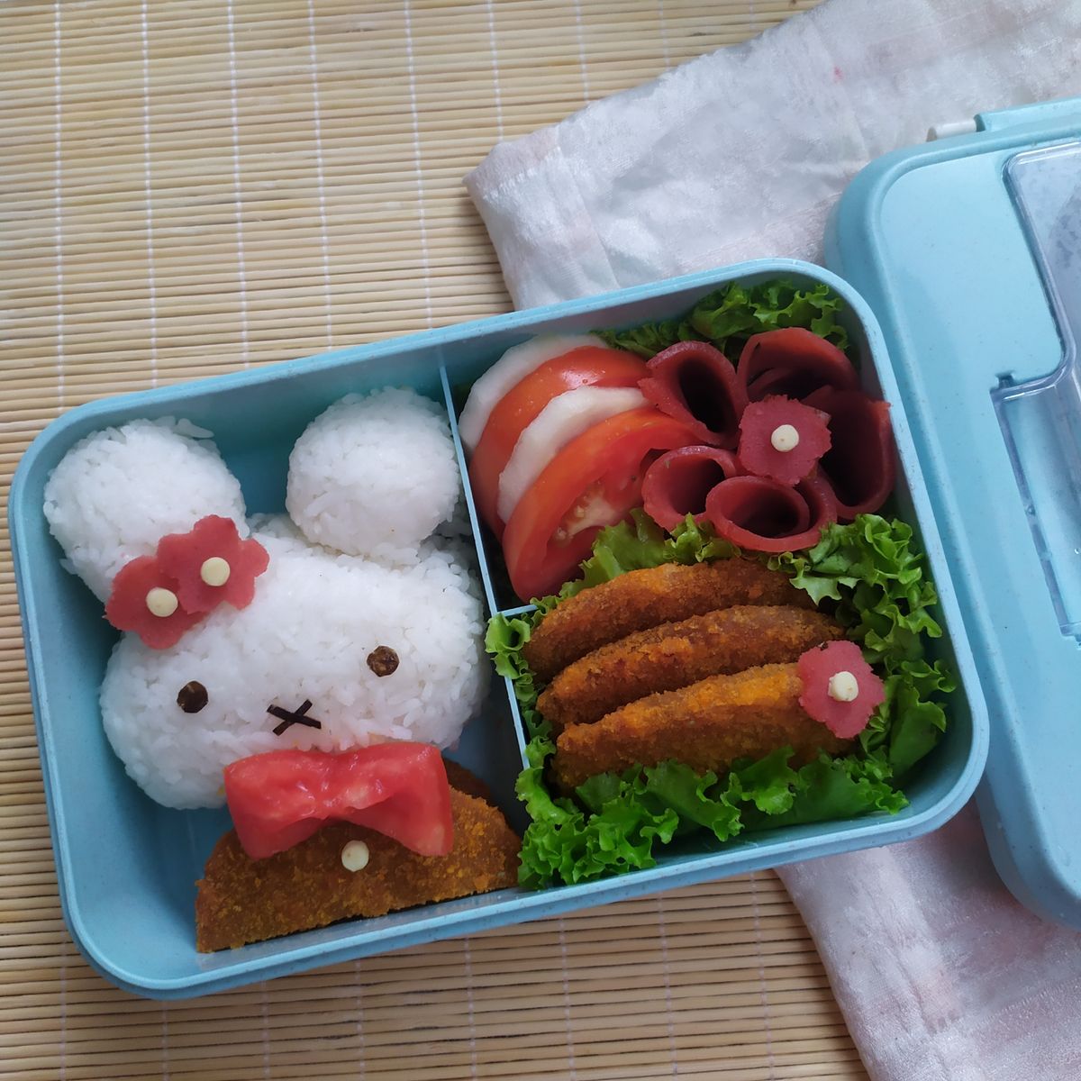Aesthetic kawaii bento box with character-shaped rice, vegetables, and fried chicken in a blue container