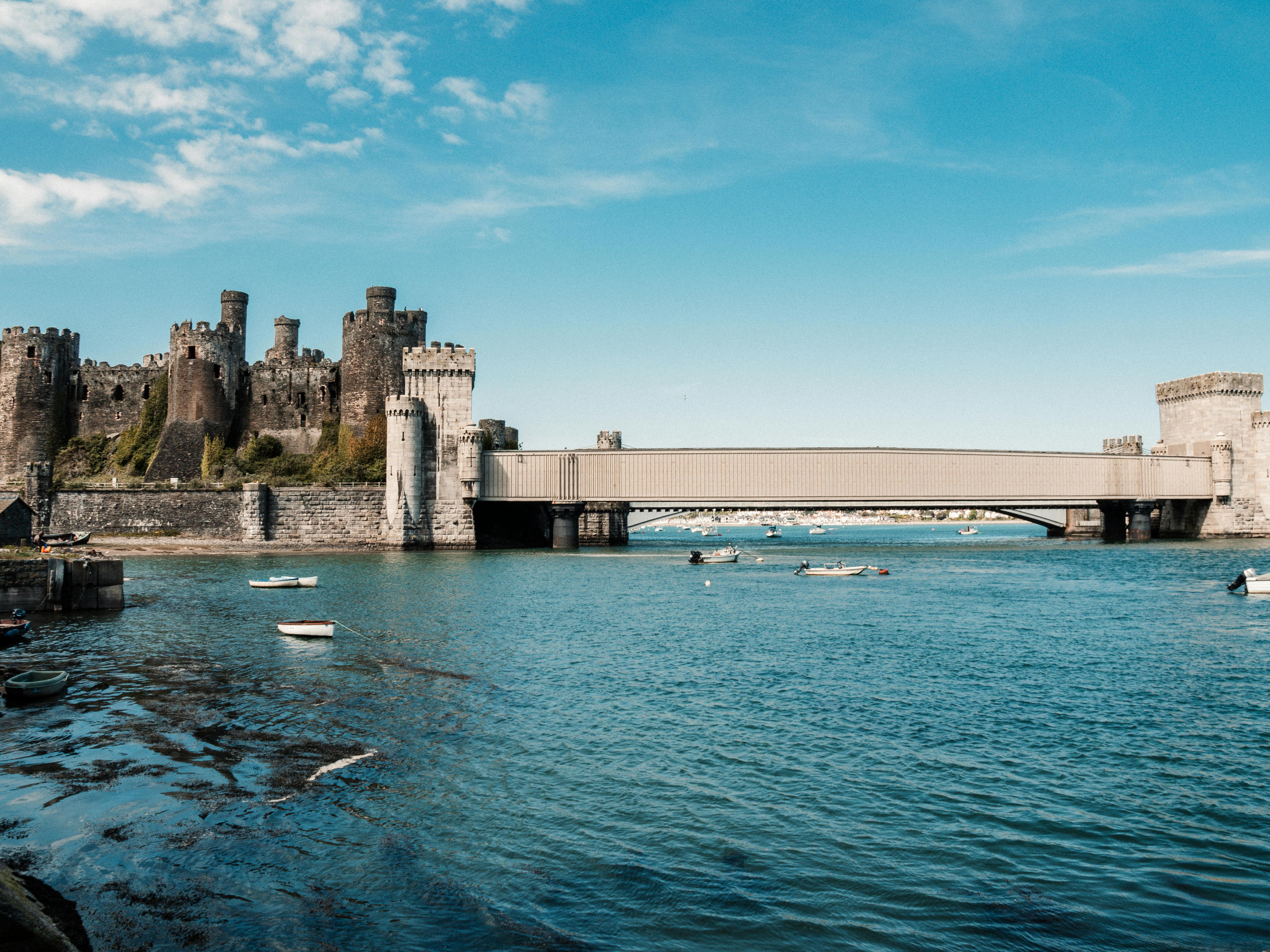 Conwy Castle in Wales overlooks a serene river and bridge under a clear blue sky.