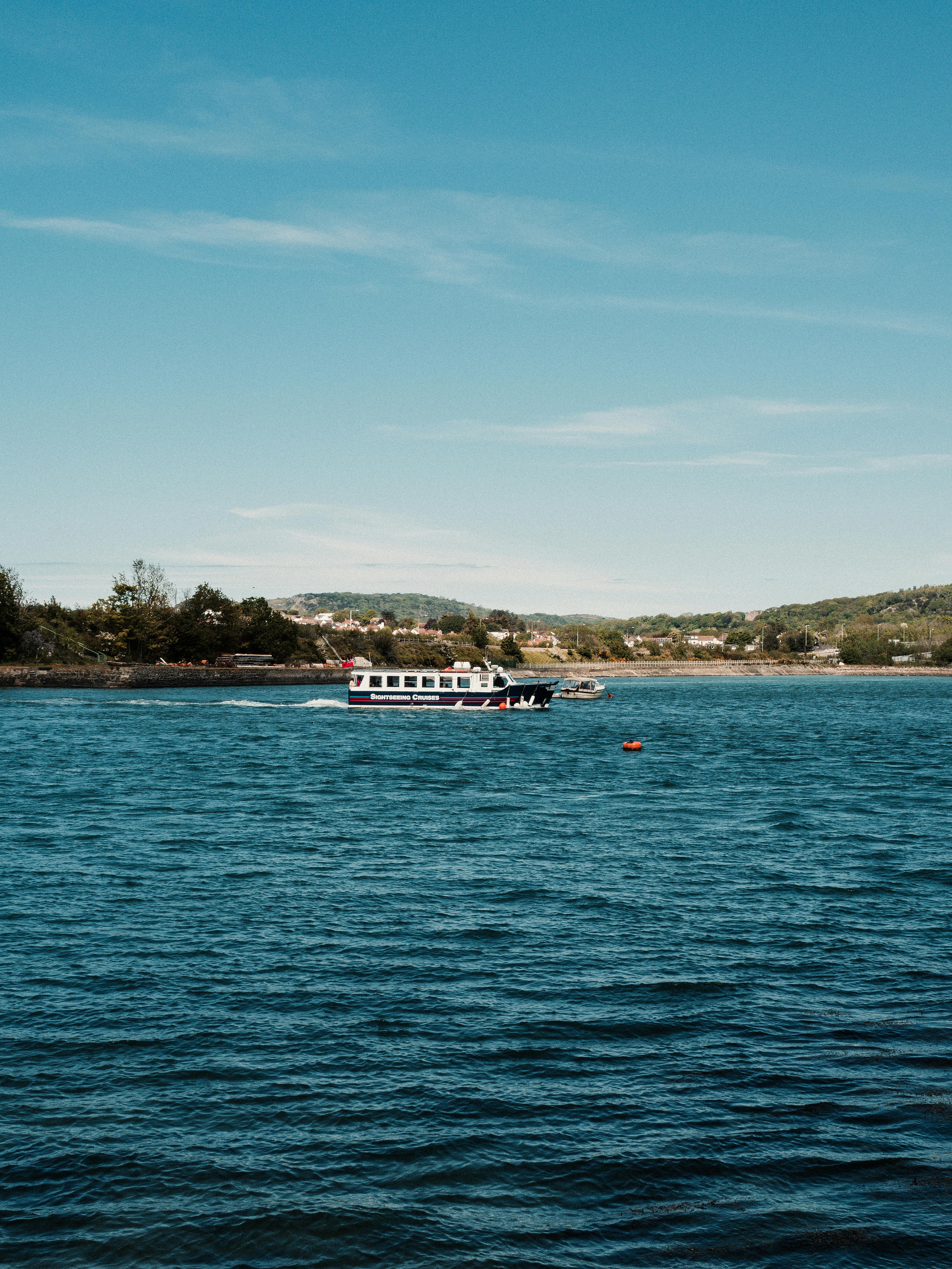 A ferry sailing across tranquil waters in Conwy with serene hills in the background.