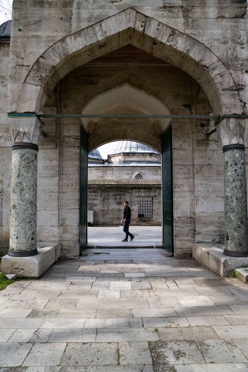 Free An adult walks past a historic stone archway in an ancient building setting. Stock Photo
