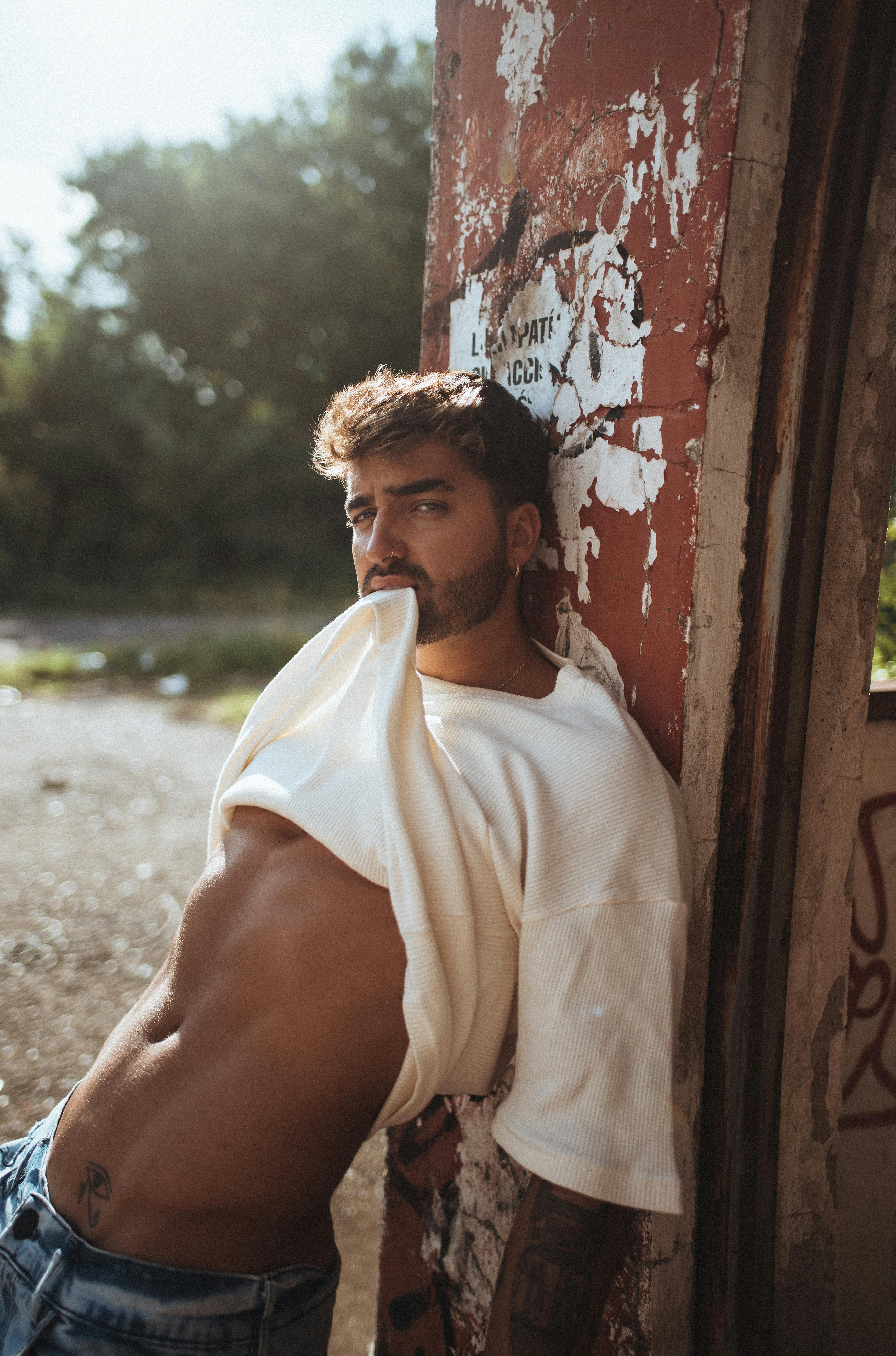 Fashionable adult man in a white shirt poses against a graffiti-covered wall outdoors.
