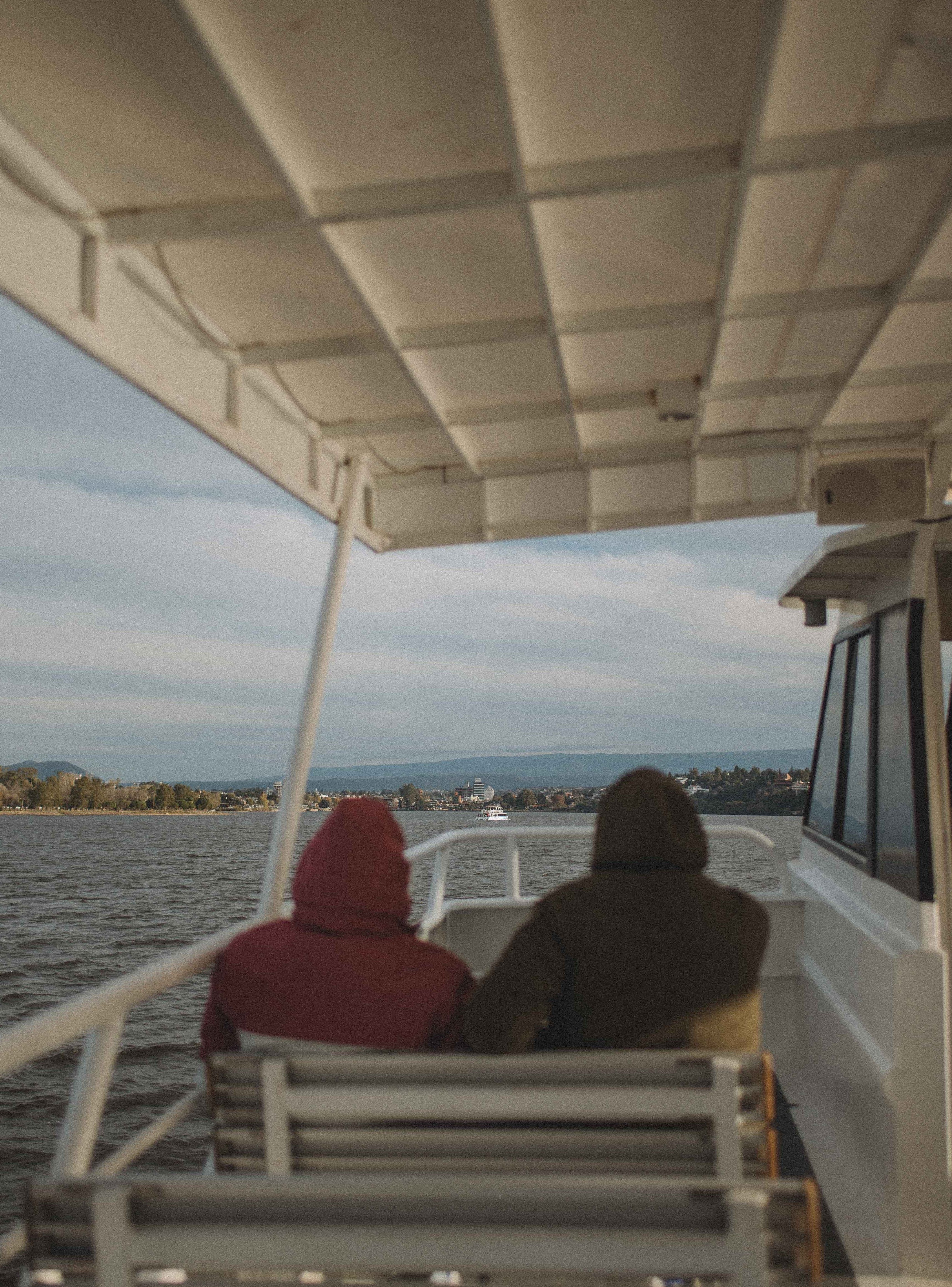 Passengers in hoodies on a scenic river cruise, enjoying the view.