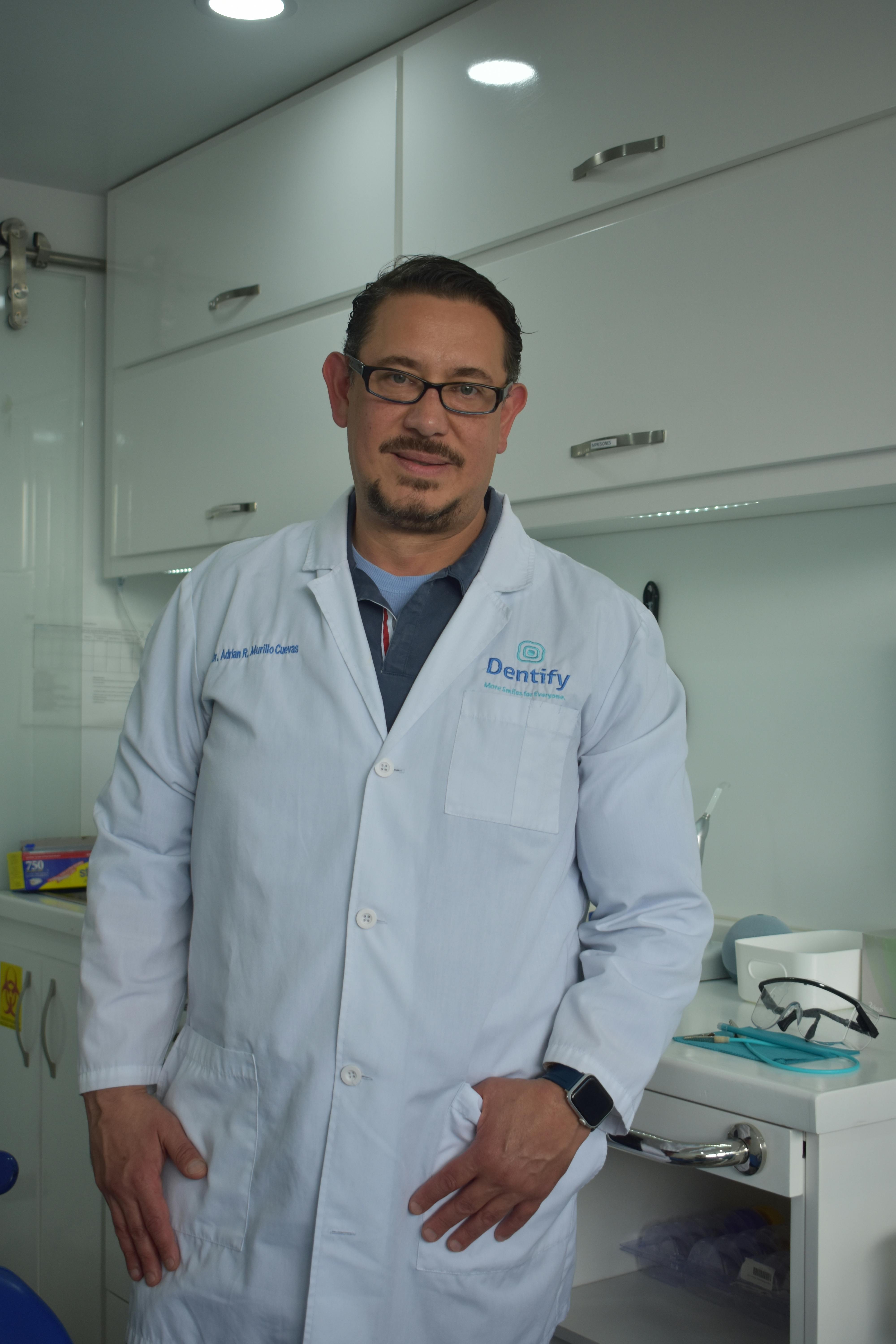 A smiling dentist stands confidently in his modern dental office, ready to assist patients.