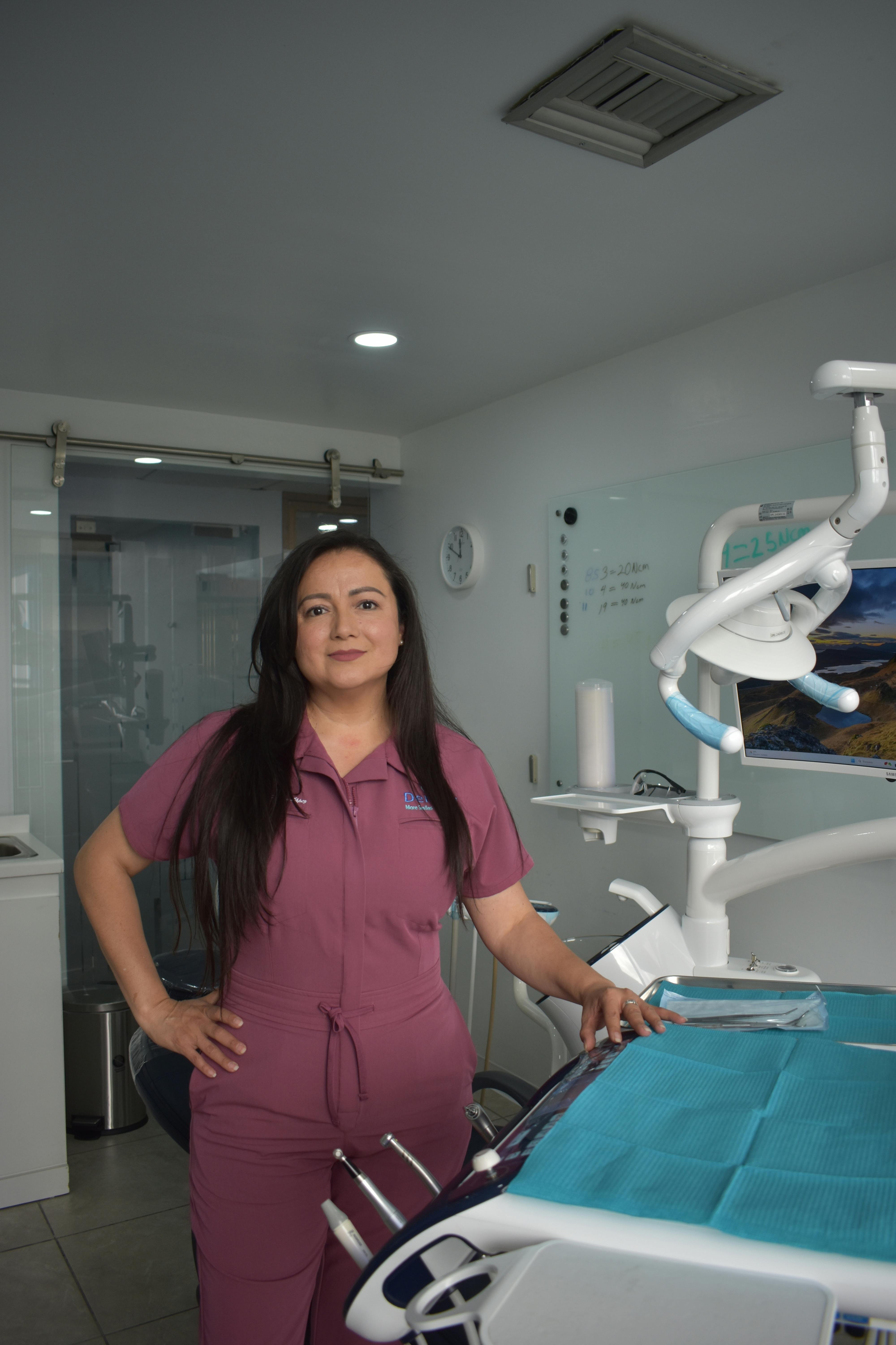 Dentist in uniform standing confidently in a bright, modern dental office setting.