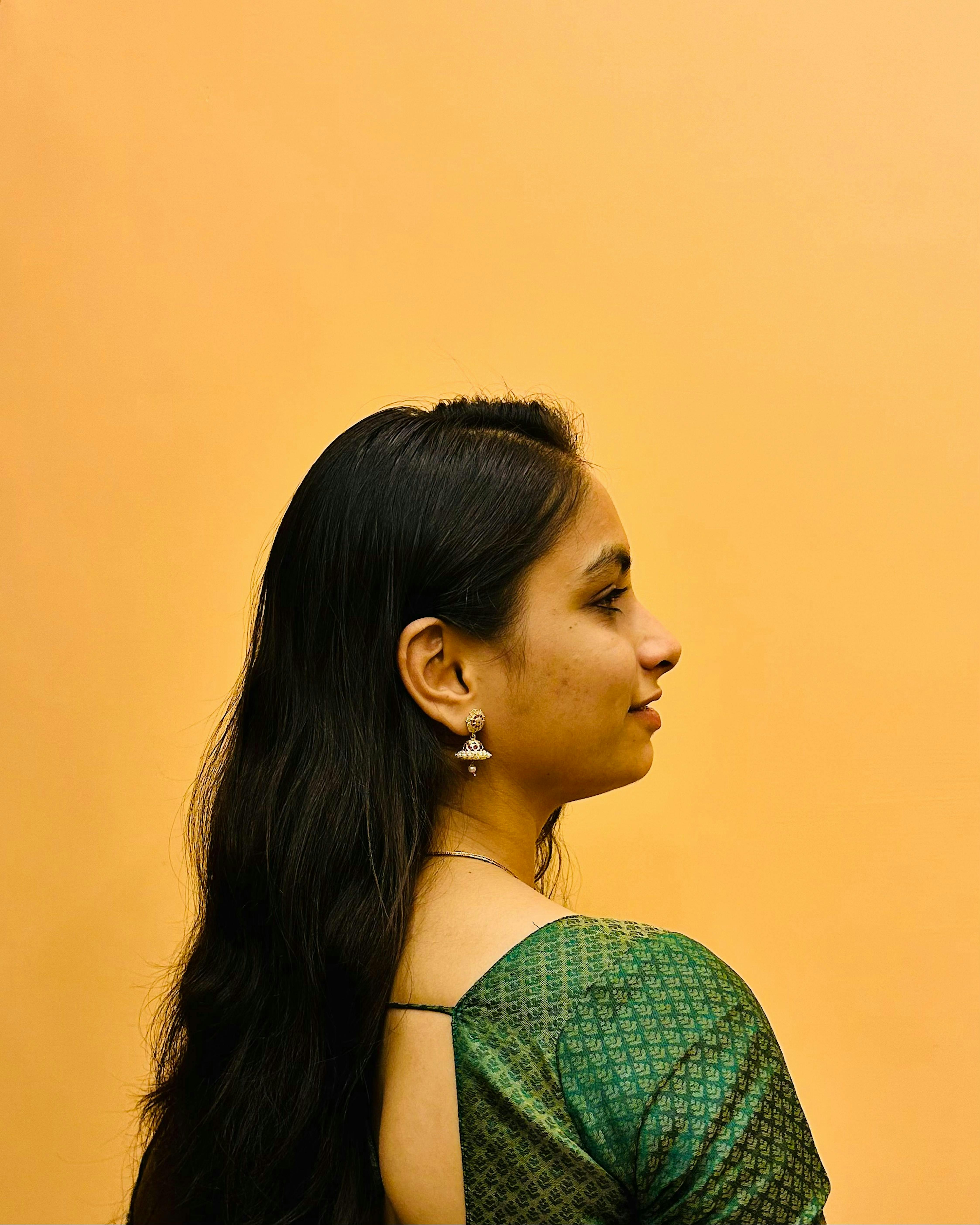 Profile view of a woman in traditional dress with elegant jewelry and long hair against a warm background.