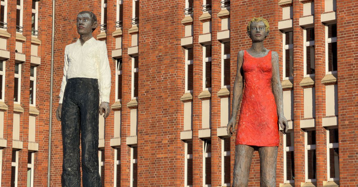 Two tall human sculptures stand prominently against a red brick building facade.
